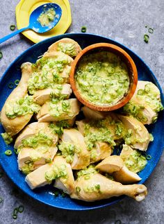 a blue plate topped with chicken covered in guacamole next to a bowl of sauce