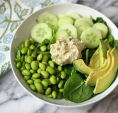 a white bowl filled with cucumbers, peas and avocado next to a fork