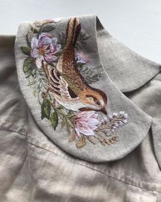 a close up of a bird on a shirt with flowers and leaves in the background