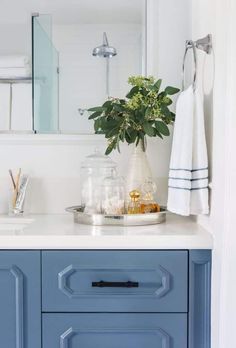 a bathroom vanity with blue drawers and white towels on the counter top, along with a plant in a vase