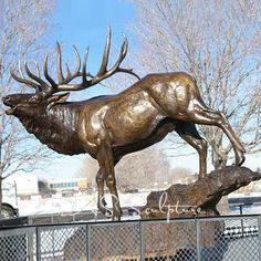 a bronze statue of a stag standing on top of a tree stump in front of a fence