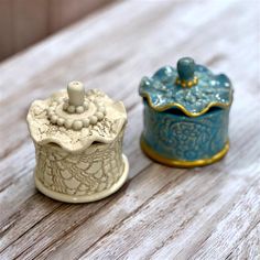 two small ceramic containers sitting on top of a wooden table with white and blue designs