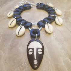 This gorgeous neckpiece is upcycled from a vegan leather belt and assembled with silver-plated/finished links, natural cowrie shells, and a batik bone mask focal. Cowie Shell, Boho Leather Jewelry, Bone Choker, Jewelry Video, Necklace African, Queen Jewelry, Big Jewelry, African Mask, Cowrie Shells