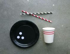 a black paper plate with two red and white striped straws on it next to a disposable cup