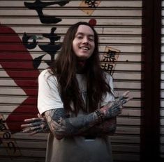 a man with long hair and tattoos standing in front of a garage door holding his hands out