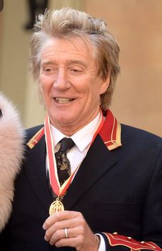 an older man in uniform holding a medal next to a white dog wearing a red and gold collar