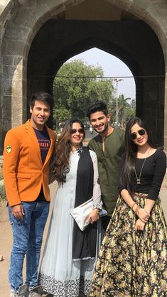 four people standing together in front of an archway