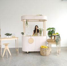 a woman standing behind a counter with lemons and potted plants in front of her