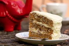 a slice of carrot cake with white frosting on a plate next to a red pig