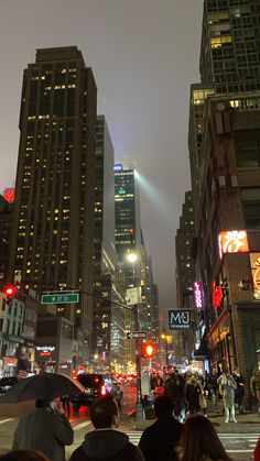 people are standing on the street in front of tall buildings at night with their umbrellas open