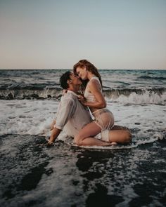 a man and woman sitting on top of a surfboard in the water at the beach