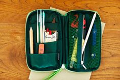 an open green case filled with pens, pencils and other items on top of a wooden table