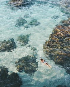 two people swimming in the ocean next to rocks