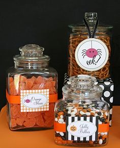 three glass jars filled with candy and candies on top of an orange tablecloth