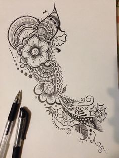 an ink drawing of a flower and paisley design on paper with two pens next to it