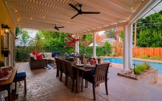 a covered patio with table, chairs and ceiling fan next to a swimming pool in the background