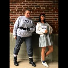 two people standing next to each other in front of a brick wall and wearing matching outfits