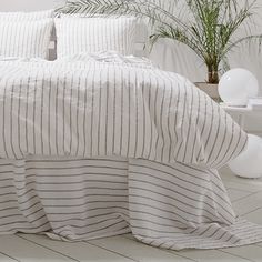 a bed with white and grey striped linens in a minimalistic bedroom setting next to a potted plant