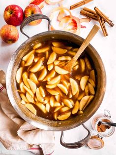 apples are being cooked in a pot with spoons and cinnamon sticks on the side