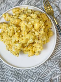 a white plate topped with macaroni and cheese on top of a table next to a fork