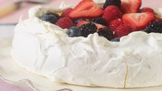 a cake with white frosting and fresh berries on top is sitting on a plate