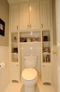 a white toilet sitting inside of a bathroom next to a wall mounted bookcases