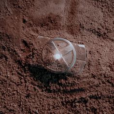 a glass bottle sitting in the dirt on top of a pile of brown sand with a light shining through it