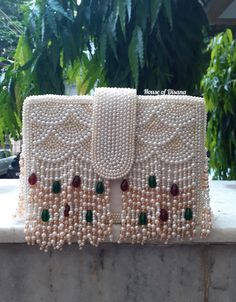 This is a beautiful handcrafted clutch bag made with love.It has intricate handwork which showcases the Indian craftsmanship by our local artisans. It comes with a pearl handle. Details  - Single side handwork  - Fabric lining on the inside to keep your belongings safe  - Magnetic lock closure  - Detachable handle  This clutch can be worn as a crossbody bag or a shoulder bag with the sling chain or can simply be carried in hand.It is spacious enough to carry mobile phones, lipsticks, Keys and ot Luxury Pouch Flap Bag With Detachable Handle, Pearl Handle Clutch As Gift, Luxury Shoulder Bag With Pearl Handle As A Gift, Luxury White Flap Bag As A Gift, Rectangular Openable Clutch For Reception, Festive Rectangular Clutch With Openable Detail, Handmade Clutch For Reception And Festivals, Festive Traditional Clutch With Pearl Embroidery, Traditional Evening Bag With Pearl Embroidery For Reception