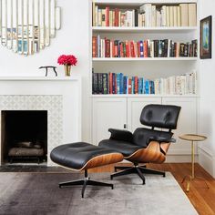 an eames lounge chair and ottoman in front of a fireplace with bookshelves