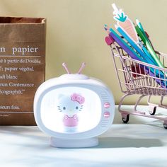 a hello kitty alarm clock sitting next to a shopping cart with pens and pencils in it