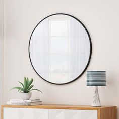 a round mirror hanging on the wall above a white dresser with a potted plant