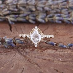 an engagement ring sitting on top of a piece of wood next to lavenders and flowers