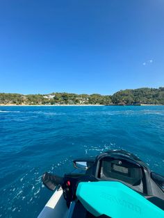 the back end of a boat in clear blue water with an island in the distance