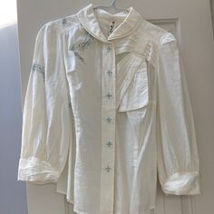 An Off-White Shirt With Blue-Green And Taupe Embroidery, Three-Quarter Sleeves, And Double Layer Round Collar. Has What Look Like Buttons But Are Actually Large Snaps Going Down The Front With Embroidered Tops. Never Worn; Still Has Extra Snaps Attached. White Collared Embroidered Shirt, Embroidered Fitted Cotton Blouse, White Embroidered Collared Shirt, Fitted Embroidered Cotton Blouse, Embroidered White Collared Shirt, White Button-up Top With Floral Embroidery, White Embroidered Button-up Top, Embroidered Cotton Collared Blouse, Fitted Long Sleeve Embroidered Cotton Top