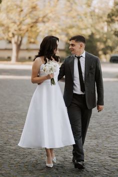 a bride and groom are walking together on the cobblestone road in their wedding attire