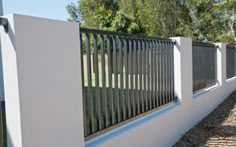 a white fence is next to a brick path and trees in the backround