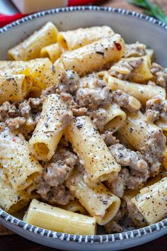 a bowl filled with pasta and meat on top of a wooden table next to cheese