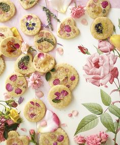 flowers and cookies are scattered on a table with pink roses in the background, as well as green leaves