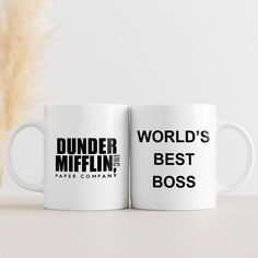 two white coffee mugs with the words dunder mifflin and world's best boss printed on them