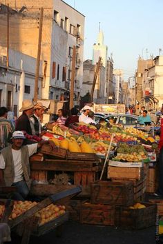 people are shopping at an outdoor market in the middle of a busy street with many fruits and vegetables on display