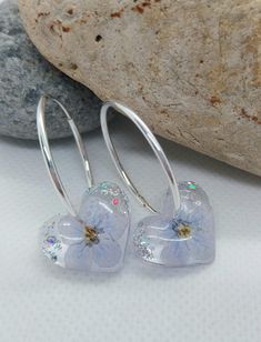 These exquisite handcrafted earrings feature real dried flowers, delicately preserved in clear resin. Each pair is truly one-of-a-kind, showcasing a unique blend of blue flowers and silver leaf, suspended on solid 925 sterling silver hoops. Details: Hoop Material: 925 Sterling Silver Hoop Size: 24mm Flower Setting: Clear Resin Please note that due to the natural variation of each flower, your earrings may differ slightly from the images shown, adding to their individual charm. For any additional Silver Drop Earrings With Pressed Flowers, Silver Sterling Flower Earrings With Pressed Flowers, Silver Pressed Flowers Drop Earrings, Silver Round Earrings With Pressed Flowers, Silver Sterling Silver Earrings With Pressed Flowers, Silver Pressed Flower Earrings In Resin, Handmade Silver Resin Flower Earrings, Silver Resin Earrings With Pressed Flowers, Silver Pressed Flower Resin Earrings