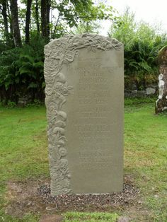 a stone monument in the middle of a grassy area with trees and bushes behind it