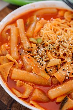 a white bowl filled with pasta and sauce on top of a wooden table next to chopsticks