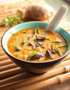 a blue bowl filled with soup on top of a bamboo mat next to garlic and mushrooms