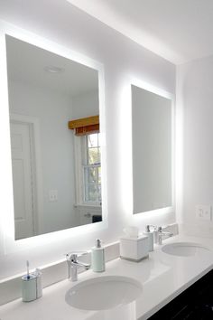 a bathroom with two sinks, mirrors and lights on the wall above them is shown