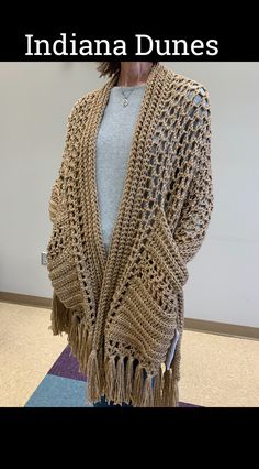 a woman standing in front of a white wall wearing a brown crocheted cardigan