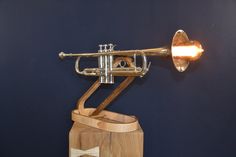 a brass trumpet sitting on top of a wooden stand next to a blue wall with a light bulb