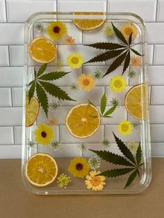 orange slices and leaves are arranged on a clear tray with white brick wall behind them