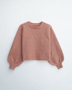 a pink sweater is hanging on a white wall and it's made out of yarn