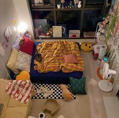 a bed sitting in the middle of a living room next to a window with lots of clutter on it